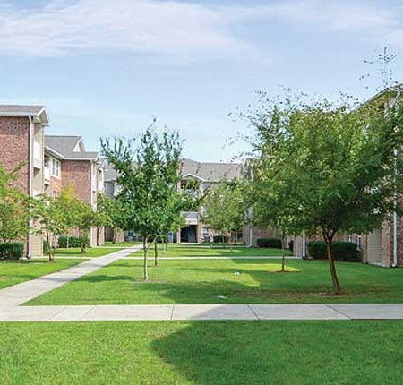 apartment buildings with green grass, trees, and a walking path at Canterbury house apartments in Baton Rouge, LA